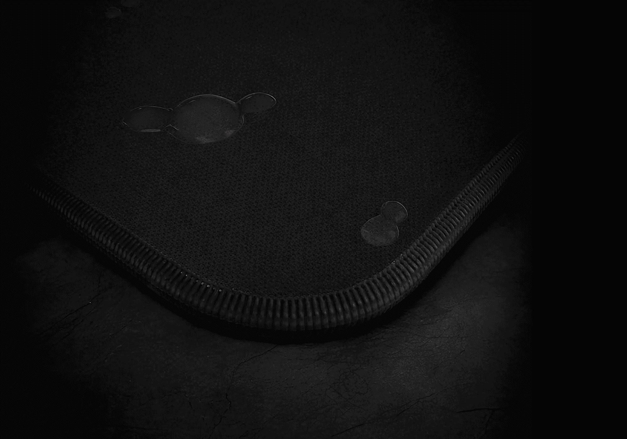 Tapis de souris gaming waterproof noir avec une surface textile résistante à l’eau et des bords cousus antidérapants.